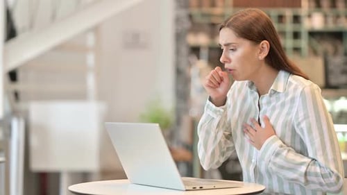 Sick Young Latin Woman with Laptop Coughing in Cafe