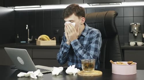 Man with runny nose working from home. Unwell male coughing at home workplace.