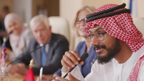 Bearded Man Speaks into Microphone at Conference Table