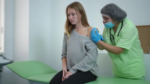 Nurse Injecting Covid19 Vaccine in Arm of Pregnant Woman Sitting on Examination Couch