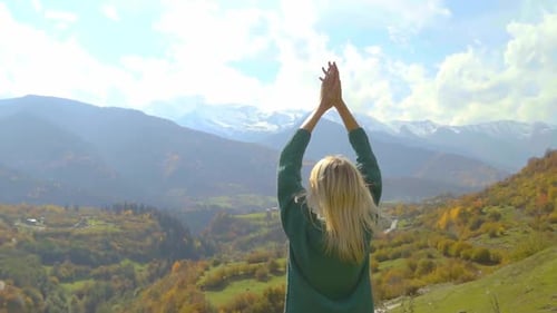 woman in denim jacket is standing on top of mountain, raising her hands in air,