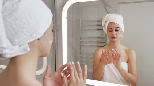 Woman Applying Lotion in Bright Bathroom Mirror
