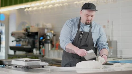 Portrait of Concentrated Caucasian Man in Apron Cutting and Weighing Raw Dough on Commercial Kitchen