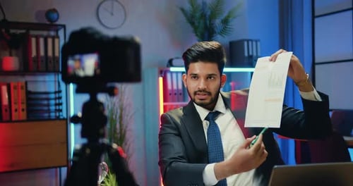 Empresario graba un vídeo para la audiencia de Internet mientras explicaba el gráfico en una moderna sala de trabajo nocturna