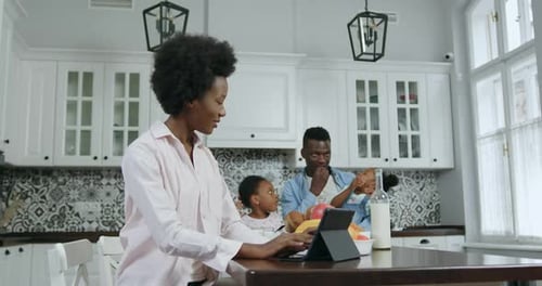 Madre afroamericana trabajando en una tableta en la mesa de la cocina