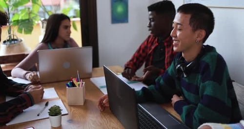 Multiracial students using laptop and digital tablet while studying together inside library