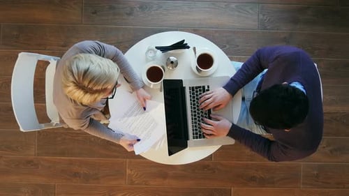 Young Business Partners Sitting at Round Table in Cafe and Working on Project