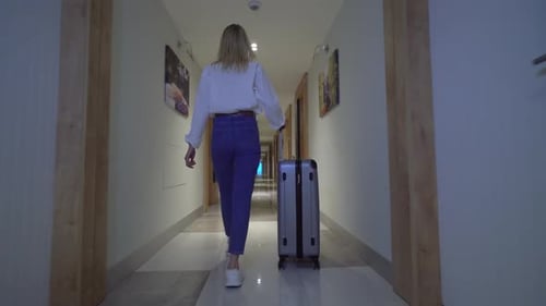 Rear view of woman walking down corridor of hotel. rolls her luggage behind her