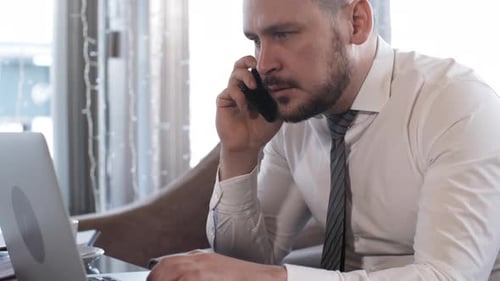 Professional Adult Working at Laptop While on Phone