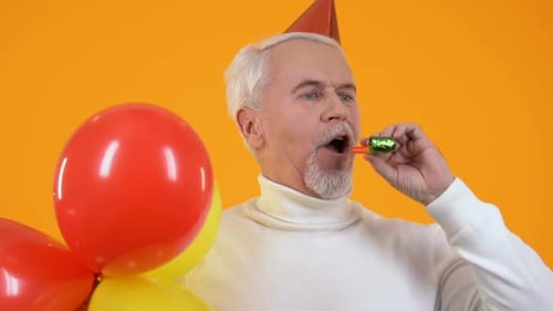 Senior Man Celebrates Birthday with Balloons and Noisemaker