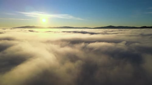 Aerial View of Vibrant Yellow Sunrise Over White Dense Clouds and Distant Mountains on Horizon