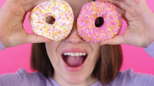 Woman Holds Doughnuts to Eyes Against Pink Background