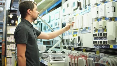 Un homme dans un magasin d'électronique choisit un système de sécurité et des alertes par interphone