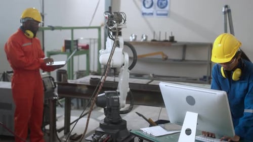 Asiatischer Ingenieur und Techniker steuern die Automatisierung des Roboterarm-Schweißens mit Computerbildschirm