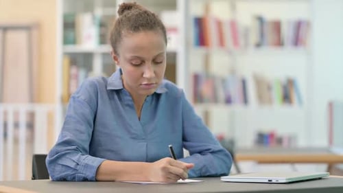 Serious Young African Woman Doing Paperwork in Library
