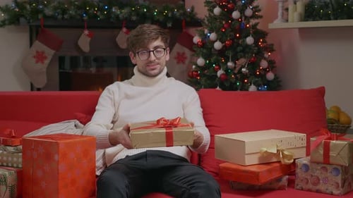 Young Man Offers Christmas Gift on Red Couch