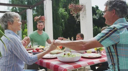 Family Gathered for Meal Holding Hands Outdoors