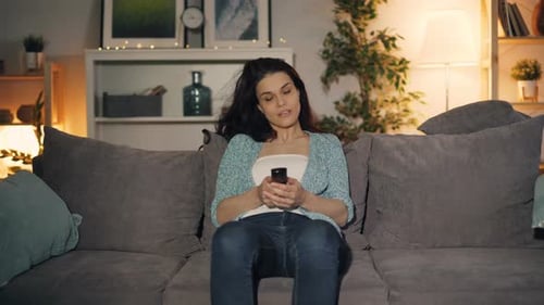 Woman Sits on Couch with Remote Control