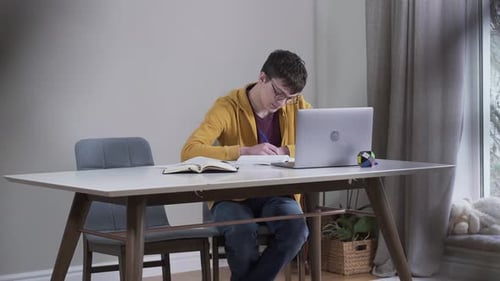 Man Studies at Desk with Computer and Notebook