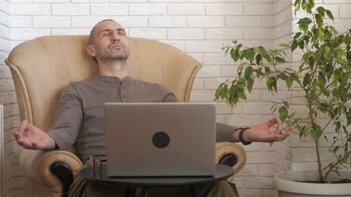 Man Meditating in Armchair with Laptop in Front