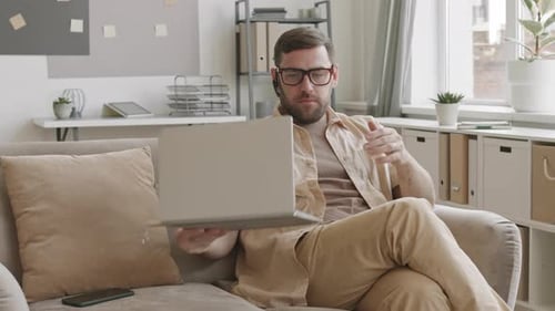 Man Works on Laptop on Couch at Home