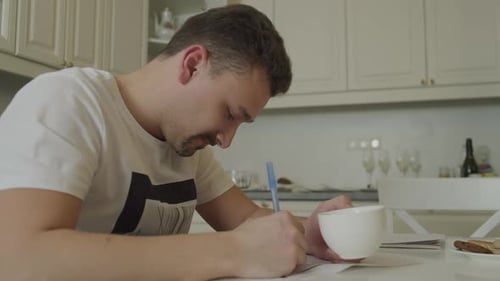 Man Writing at Kitchen Table During the Day