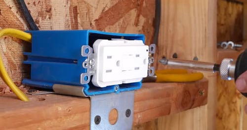 An electrician construction worker using a power drill to install an electrical outlet in a new home