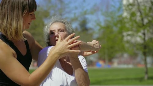 Focused Elderly Lady with Coach Stretching Arm in Park