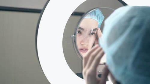 Young Woman Adjusting Eyebrows in Ring Light Mirror