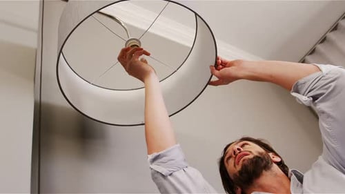 Man Installs Lightbulb and Lampshade in Living Room