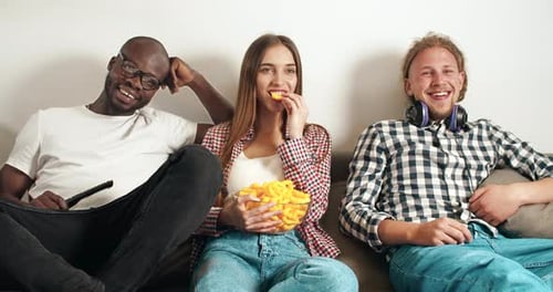 Laughing Friends Watch TV and Eat Chips Indoors