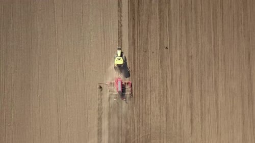 Top down aerial view of green tractor cultivating ground and seeding a dry field.