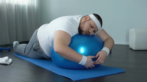Gros homme à faible volonté se relaxant sur un ballon de fitness, pause d'entraînement à la maison, paresse