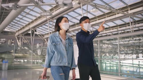 Asian Man and woman passengers wearing face mask walking in airport terminal to boarding gate.