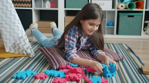 Cute Kid Playing with Toys Lying on Carpet in Children's Room Concentrated on Interesting Game