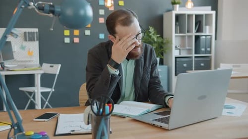 Tired Guy Working with Laptop Computer in Office Suffering From Headache Overworking