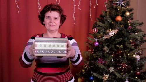 Woman Presents Christmas Gift in front of Tree