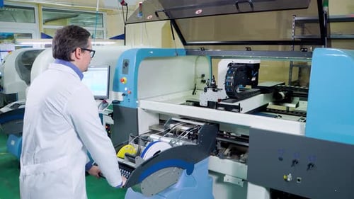 Der Ingenieur in einem weißen Gewand und einer Brille arbeitet für die Surface Mount Technology Machine, PCB