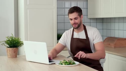Young Man Eating Salad While Using Laptop