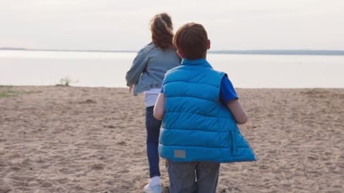 Two Children Run Along Sandy Beach To Seashore