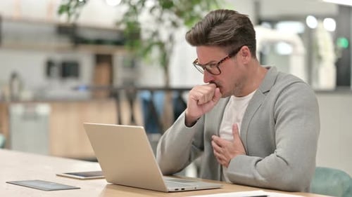 Sick Middle Aged Man with Laptop Coughing in Office