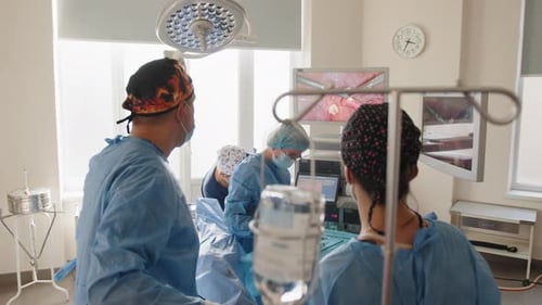 Back View of Surgeons Team Looks at Monitors While Preforming Operation in