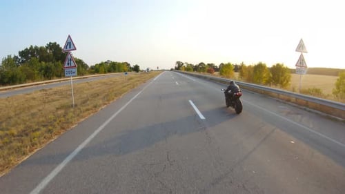 Follow to Biker Riding on Modern Sport Motorbike at Highway During Sunny Autumn Day