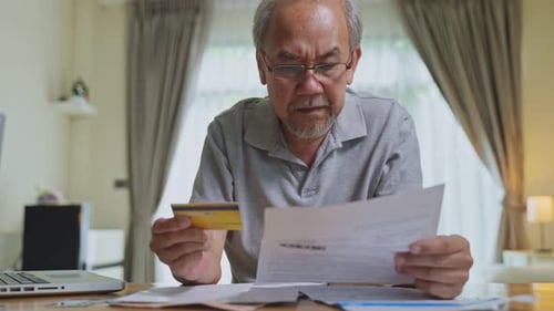 Depressed desperate Asian Senior Elderly male look at bills feeling worried about financial problem.