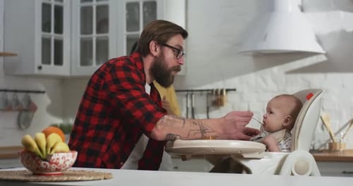 Father Feeding Baby in High Chair at Home