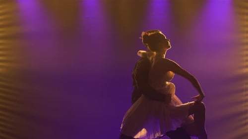 Couple of Ballroom Dancers are Dancing Romantically in a Dark Studio Against the Backdrop of Bright