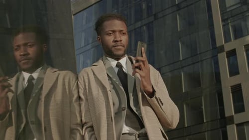 Man in Suit Using Phone By Reflective Building