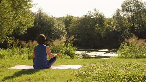 Woman Meditating in Nature near a River