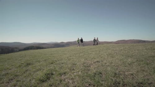 Adults and Dog Hiking Together in Grassy Field