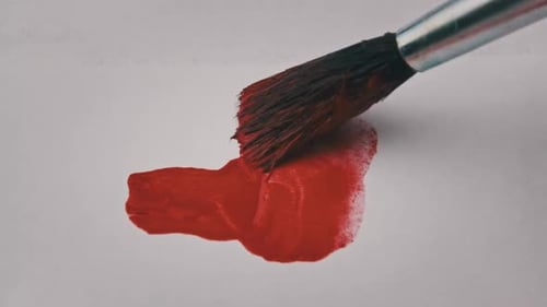 Pinsel mit roter Farbe zeichnet im Makro eine Linie auf weißem Papier